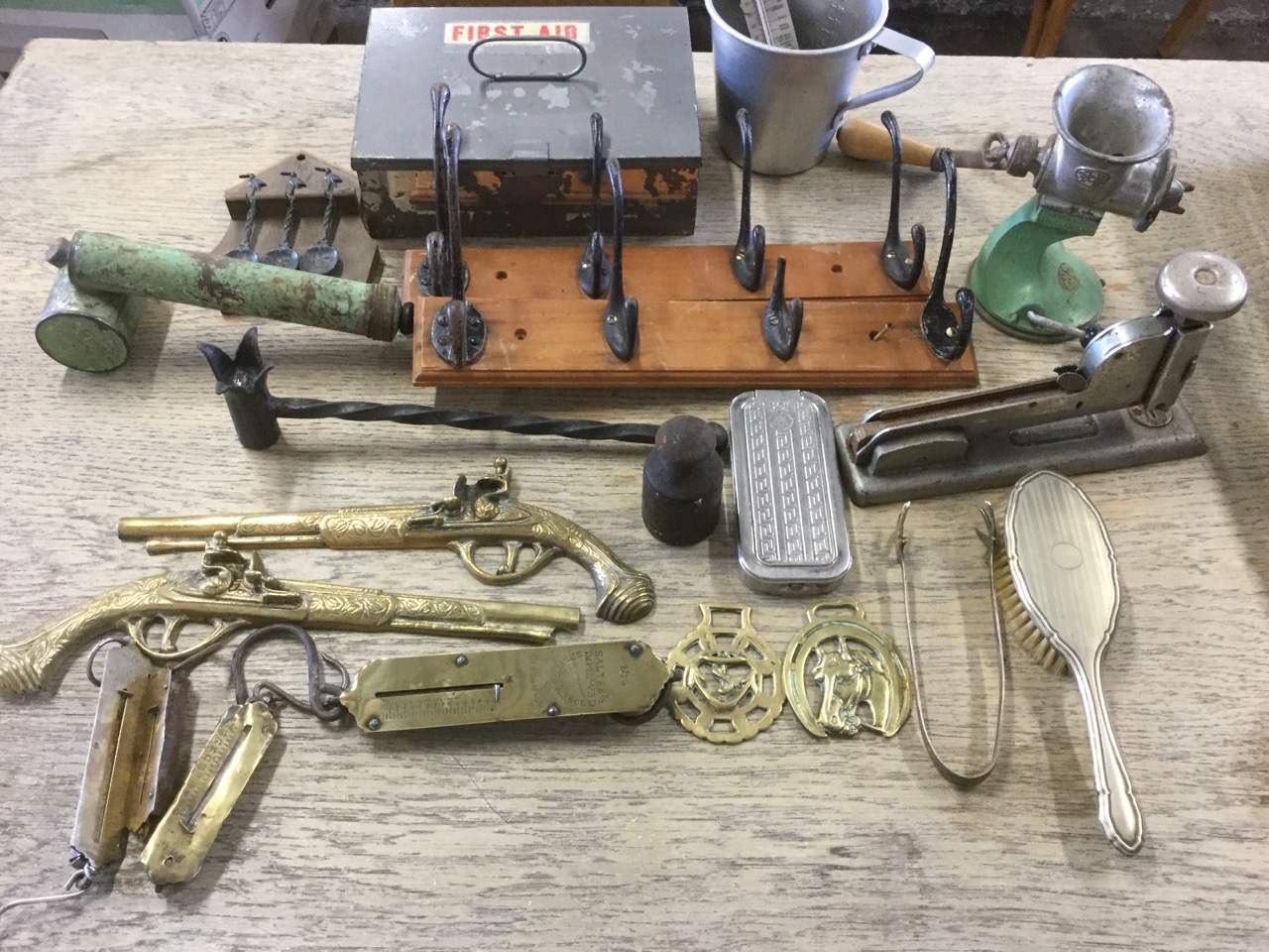 A box of miscellaneous items including rows of pegs, a mincer, four brass Salter scales, a spoon