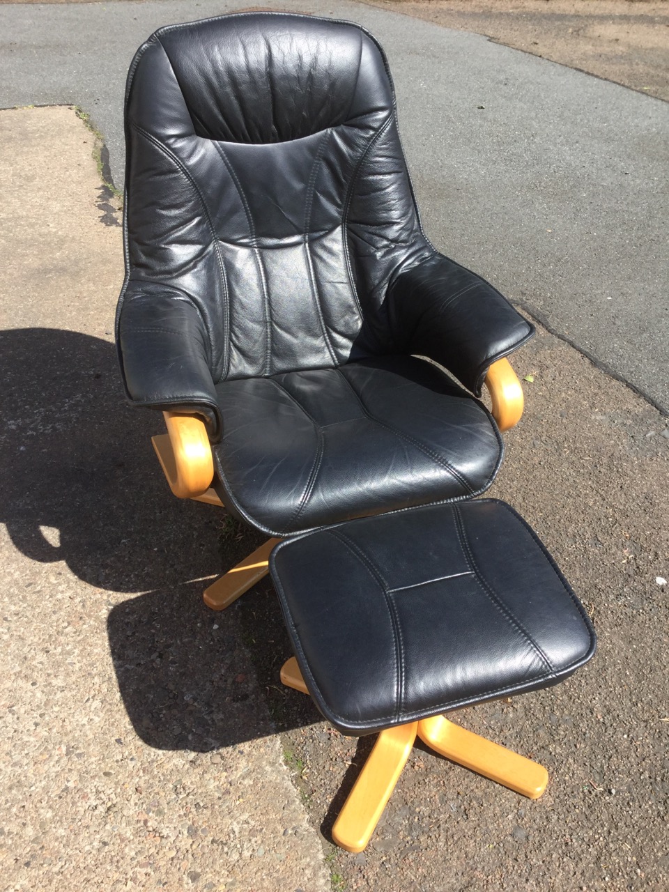 A modern leather upholstered armchair and footstool, with panelled back, seat and arms, supported on