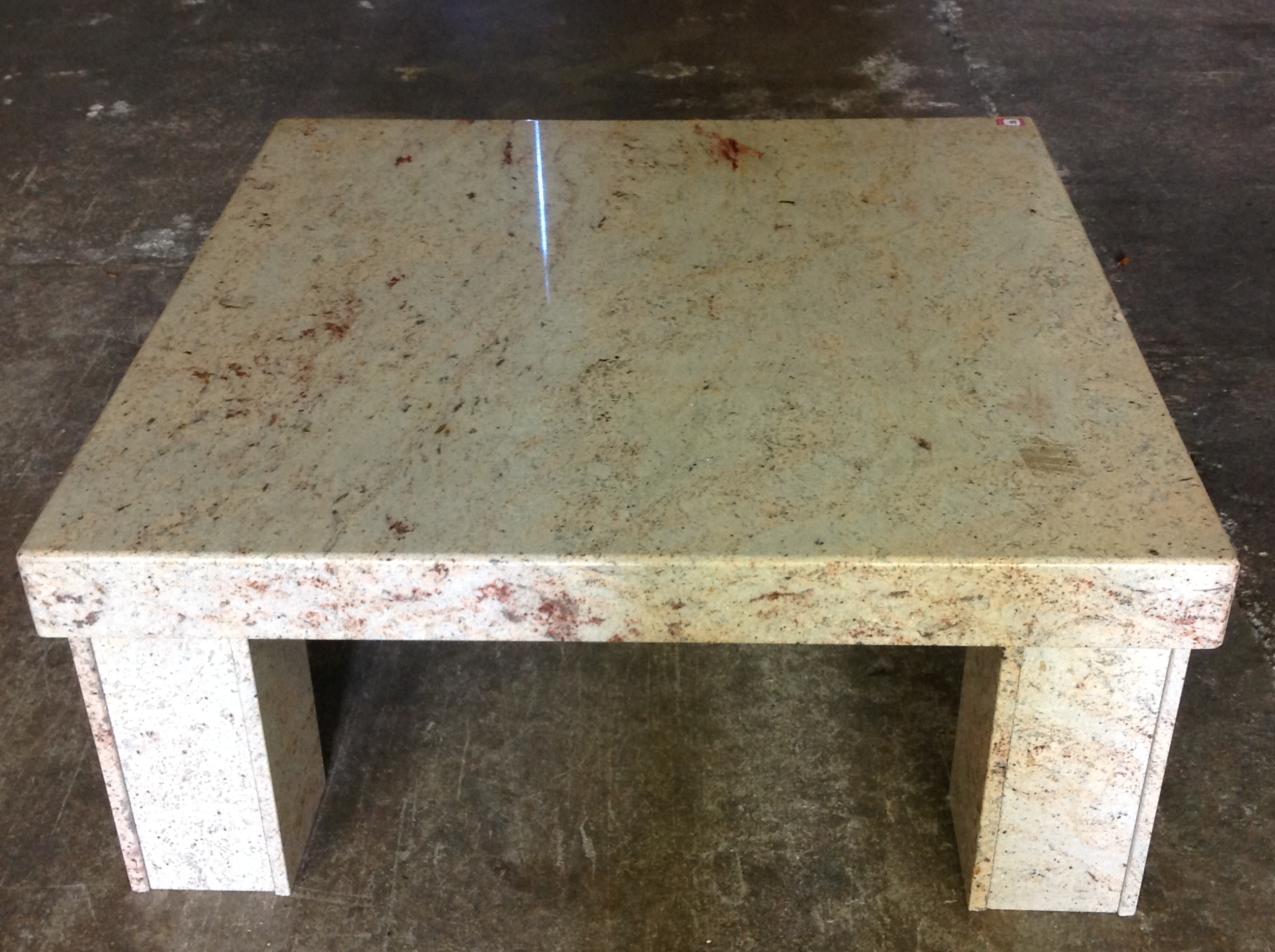 A large polished granite coffee table, the square slab top supported on four channelled column legs.