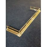 A brass fender, the moulded curb mounted with tubular rail on gallery columns, the corners with