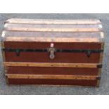 A seamans trunk with domed lid having wood slats & brass mounts, the box on casters.