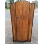 A walnut wardrobe with bowfronted quarter-veneered arched door, enclosing hanging space and shelves.