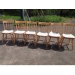 A set of six beech kitchen chairs with angled slatbacks above solid seats with cushions, raised on