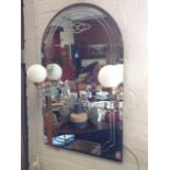 An arched mirror with bevelled cut decoration, mounted with milk glass ball lights on brass brackets