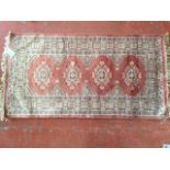 An oriental silk style rug, woven with four lozenges on salmon pink field, framed by flowerhead