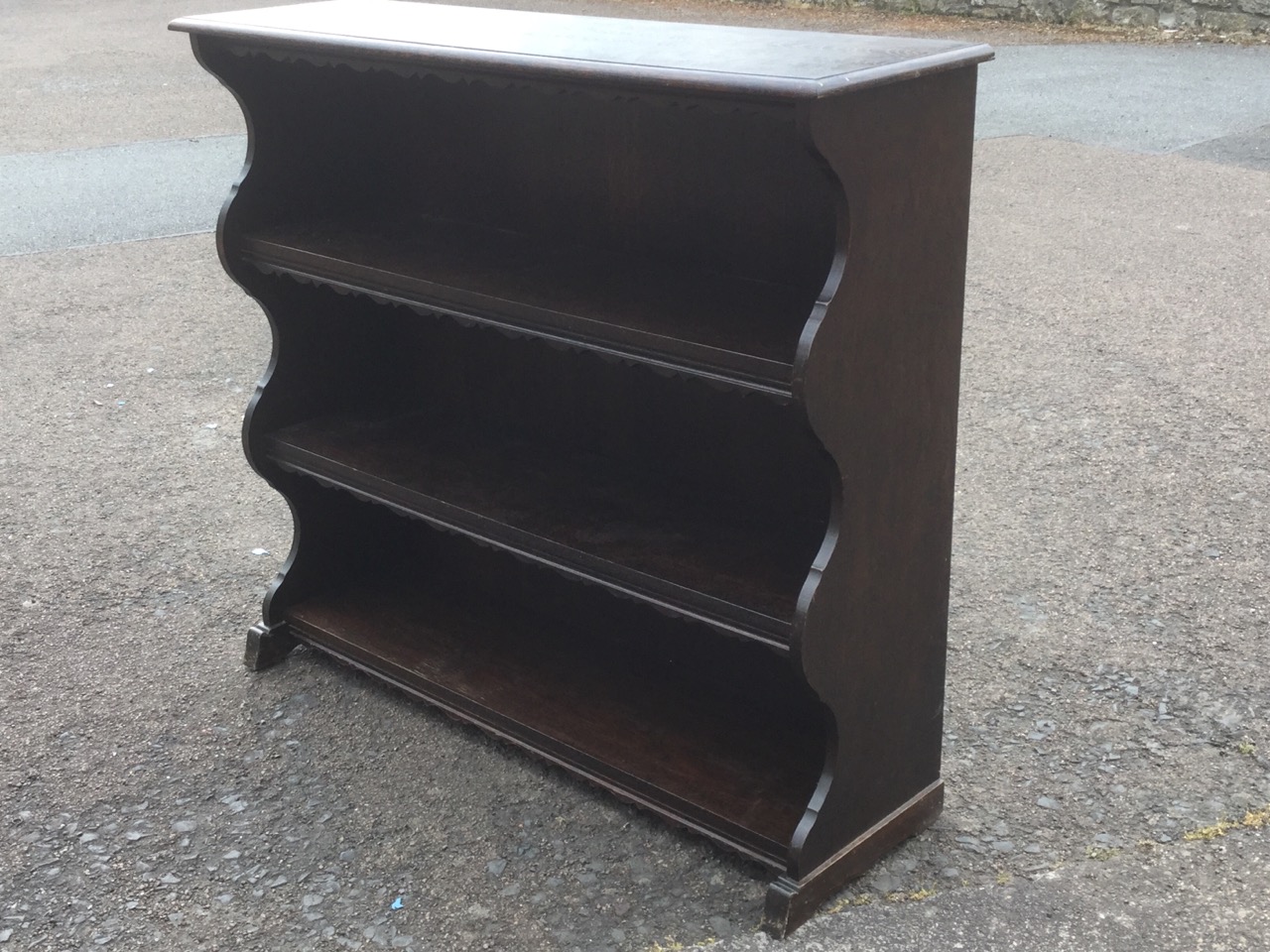 An oak open bookcase, the moulded shelves with shaped aprons, with waved sides.