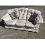 A three-seater sofa with floral tapestry style button upholstery and loose cushions with padded arms