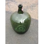 An antique green glass carboy, the vessel with indented base and tapering tubular neck.