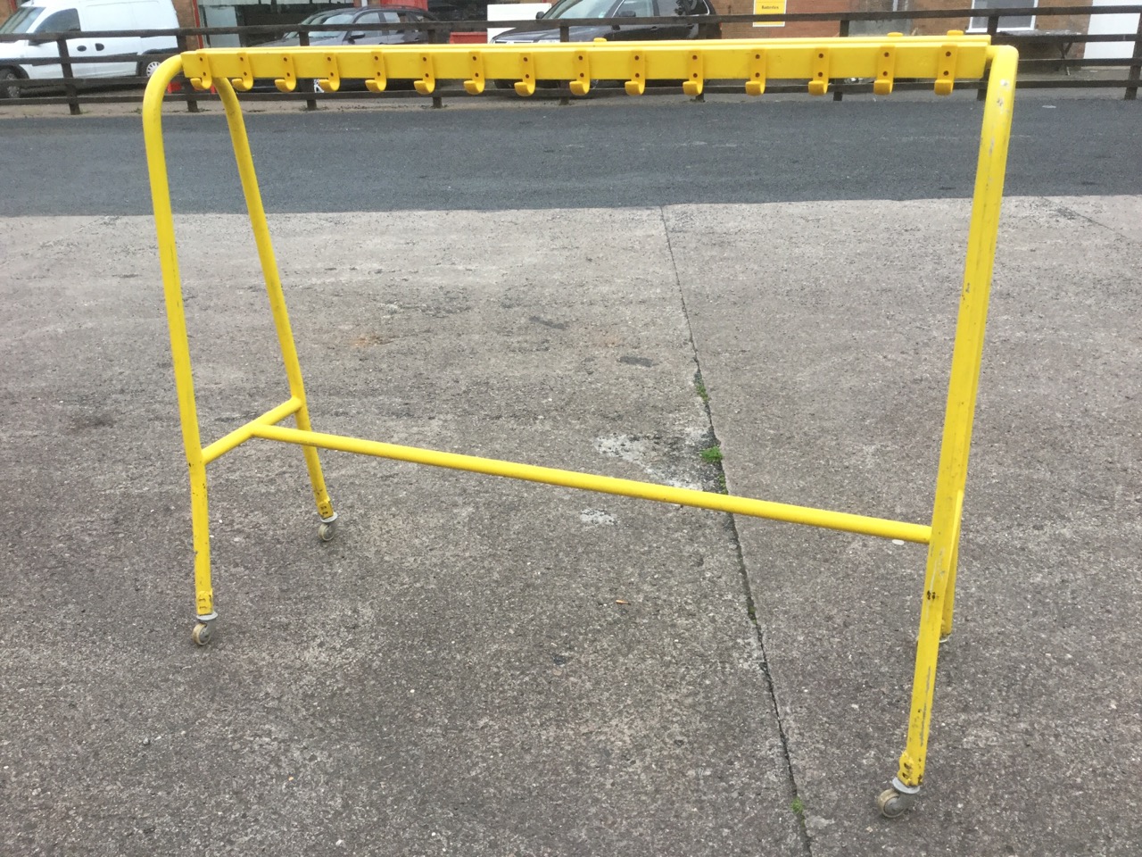 A painted school coatstand, with hooped supports on casters holding batons with pegs.