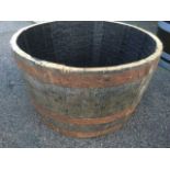 An oak barrel tub planter, the staves bound by three metal strap bands.