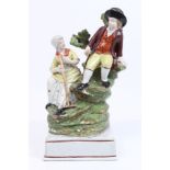 Late 18th century pearlware figure group of a boy with sickle and girl with rake on rocky outcrop,