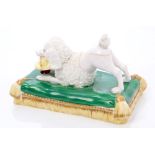 Minton poodle, circa 1830, in playful pose with basket in mouth, lying on a tasselled cushion base,