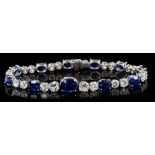Sapphire and diamond bracelet with a graduated line of oval mixed cut blue sapphires interspaced by