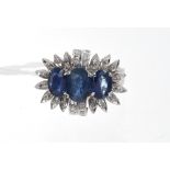 Sapphire and diamond cocktail ring with three oval mixed cut blue sapphires within a border of