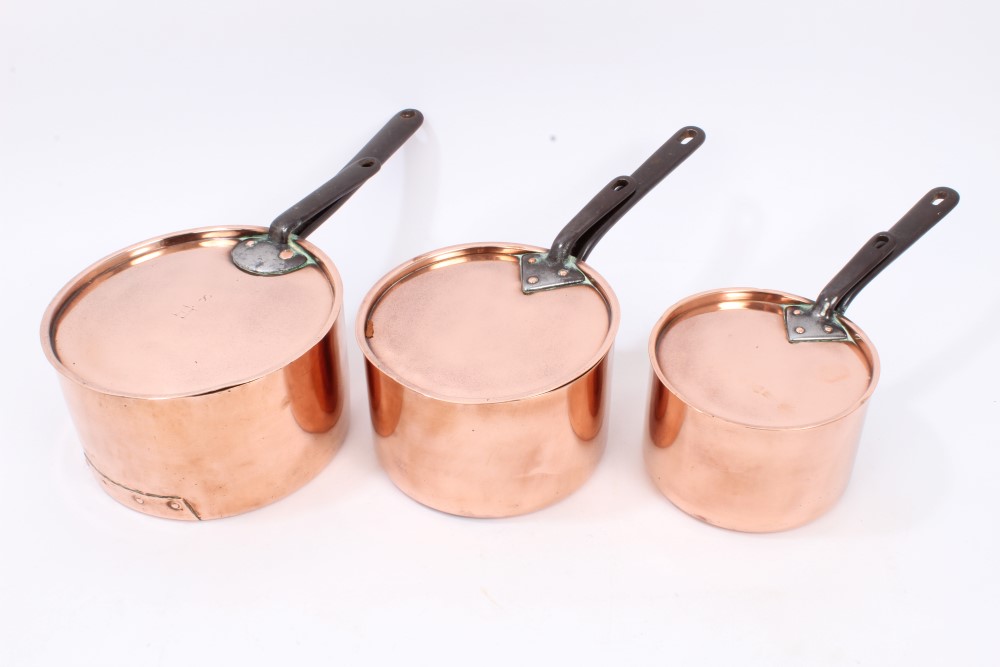 Graduated set of three copper saucepans and covers, each with pierced iron handles,