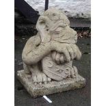 A concrete garden statue of a gargoyle holding an armorial