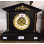 A late Victorian black slate cased mantel clock of architectural design with brass mask, flanking