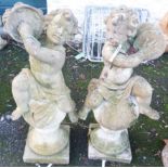 A pair of 3' 2" concrete garden statues depicting putti playing symbols and sat atop finial bases