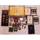 A cigar box containing a various commemorative crowns and coin sets, .999 ounce of silver ingot,