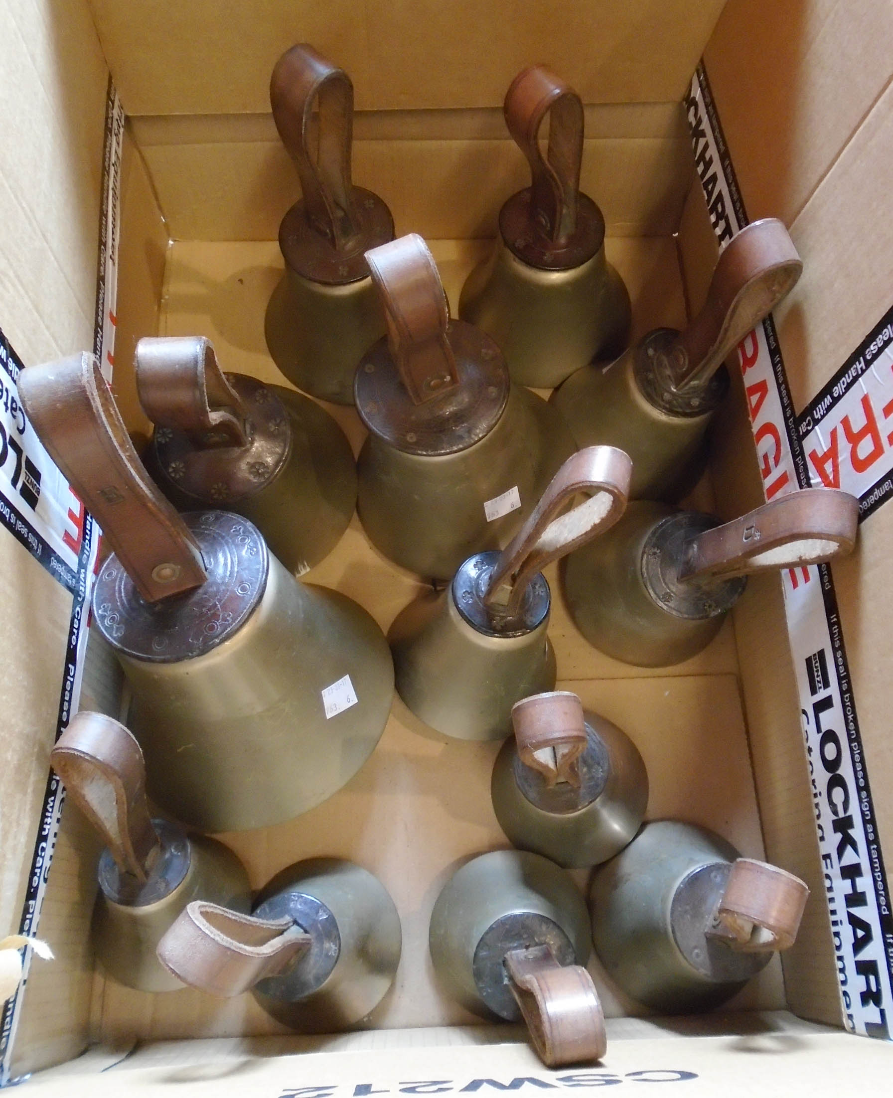 A box containing thirteen consecutive tuned bell metal handbells with embossed leather handles,