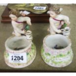 A pair of continental dressing table tidies with cherub figures and painted decoration to inside