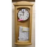 A modern blonde wood cased pendulum wall clock with battery movement
