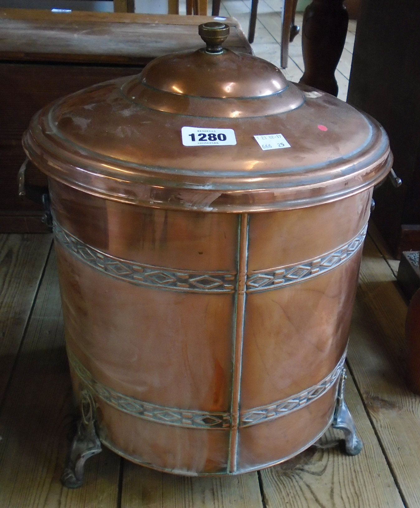 A copper two handled lidded coal bucket with two bands of embossed decoration, set on claw feet