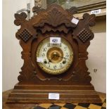 An American stained oak framed gingerbread shelf clock with decorative dial and Ansonia gong