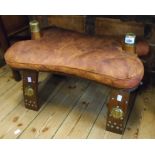 An Egyptian souvenir camel saddle stool with leather swab cushion, embossed brass plaques