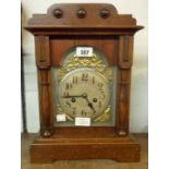 A stained oak cased mantel clock with decorative dial, flanking half columns and eight day gong