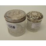 Two silver topped dressing table jars, one with cherub decoration, the other C-scrolls