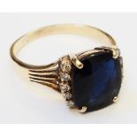 An unmarked yellow metal ring, set with central large cushion cut sapphire within flanking rows of