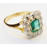 A marked 18ct. yellow metal ring, set with central emerald within a ten stone diamond border