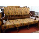 A 5' 6" oak show frame settee with spindle back, studded repeat pattern upholstery, scroll