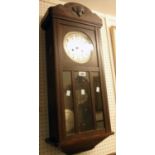 An early 20th Century stained oak cased wall clock with visible pendulum and eight day gong striking