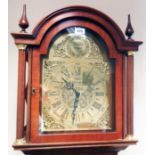 A reproduction stained wood longcase clock with decorative arched brass dial, visible pendulum and