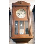 An early 20th Century stained oak cased wall clock with visible pendulum and eight day gong striking