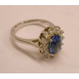 A platinum ring, set with central oval sapphire within a twelve stone diamond border