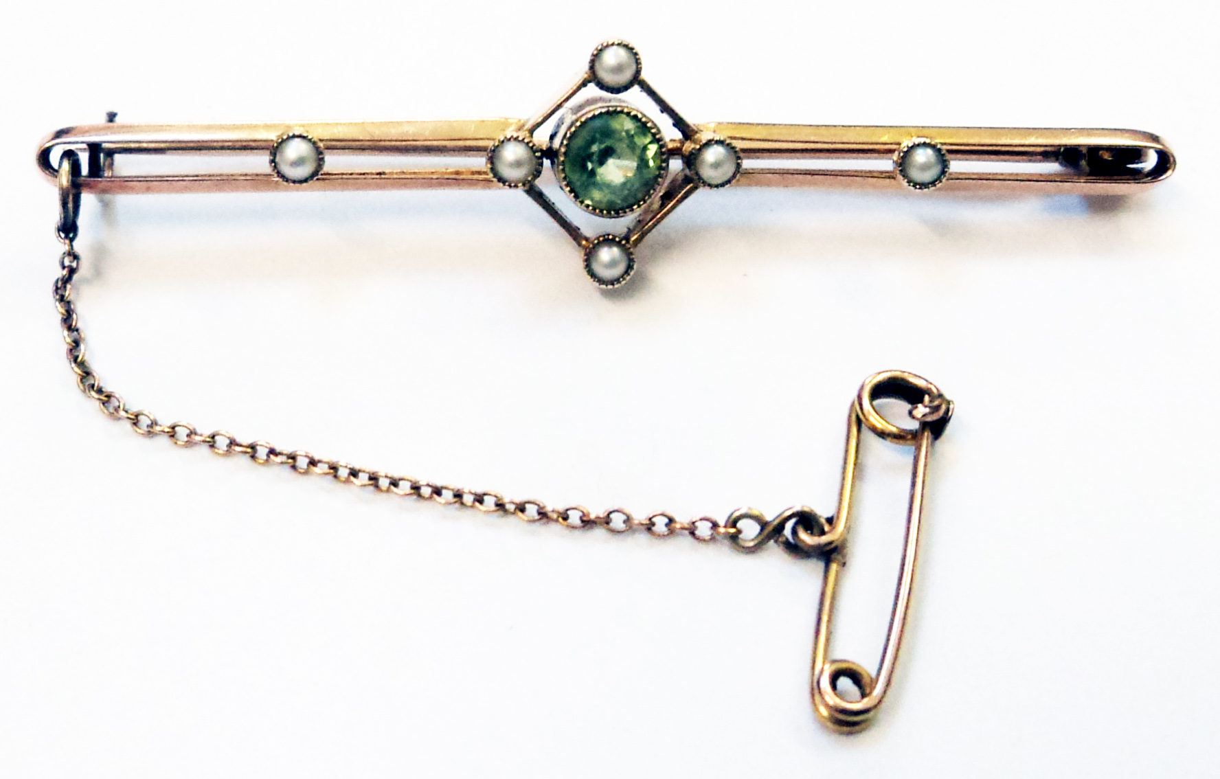 An early 20th Century 9ct. gold bar brooch with open set central peridot, six seed pearls and safety