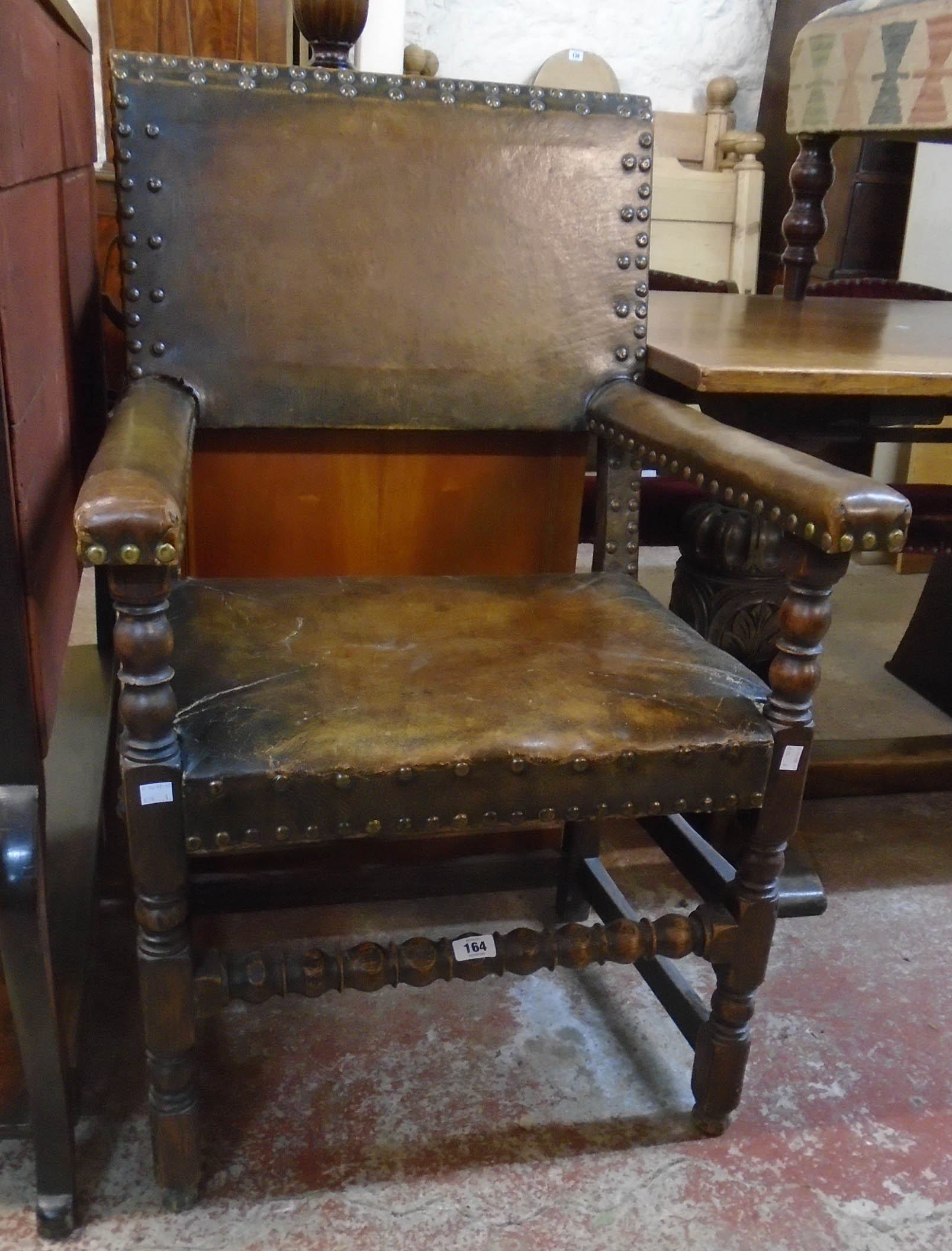 A stained oak framed elbow chair with studded brown leather upholstery to back, armrests and seat,