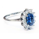 A platinum ring, set with central oval sapphire within a twelve stone diamond border