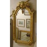 A modern ornate gilt and stained framed wall mirror with mask, floral and acanthus scroll decoration