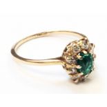 A yellow metal ring, set with a central oval emerald within a diamond border