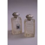 A PAIR OF SILVER LIDDED GLASS SCENT BOTTLES, having embossed floral and scroll detail top