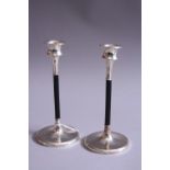 A PAIR OF SILVER CANDLESTICKS, having circular weighted silver foot to ebonised support with