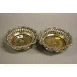 A PAIR OF SILVER BOTTLE COASTERS, having fluted interior border to shaped beaded and scrolled