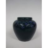 A RUSKIN POTTERY OVOID VASE AND COVER, having trailing blue flowers and leafage decoration to dark