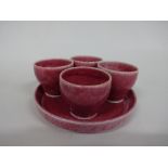 FOUR RUSKIN POTTERY EGG CUPS, on circular stand having tonal red crystalline glaze, all impressed