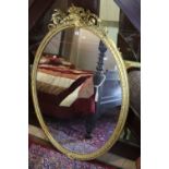 A MID VICTORIAN GILT FRAMED OVAL WALL MIRROR, the cresting in the form of flowers and leaves flanked