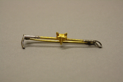 A 9CT GOLD AND SILVER BAR BROOCH, in the form of a riding crop with fox's mask to centre, length